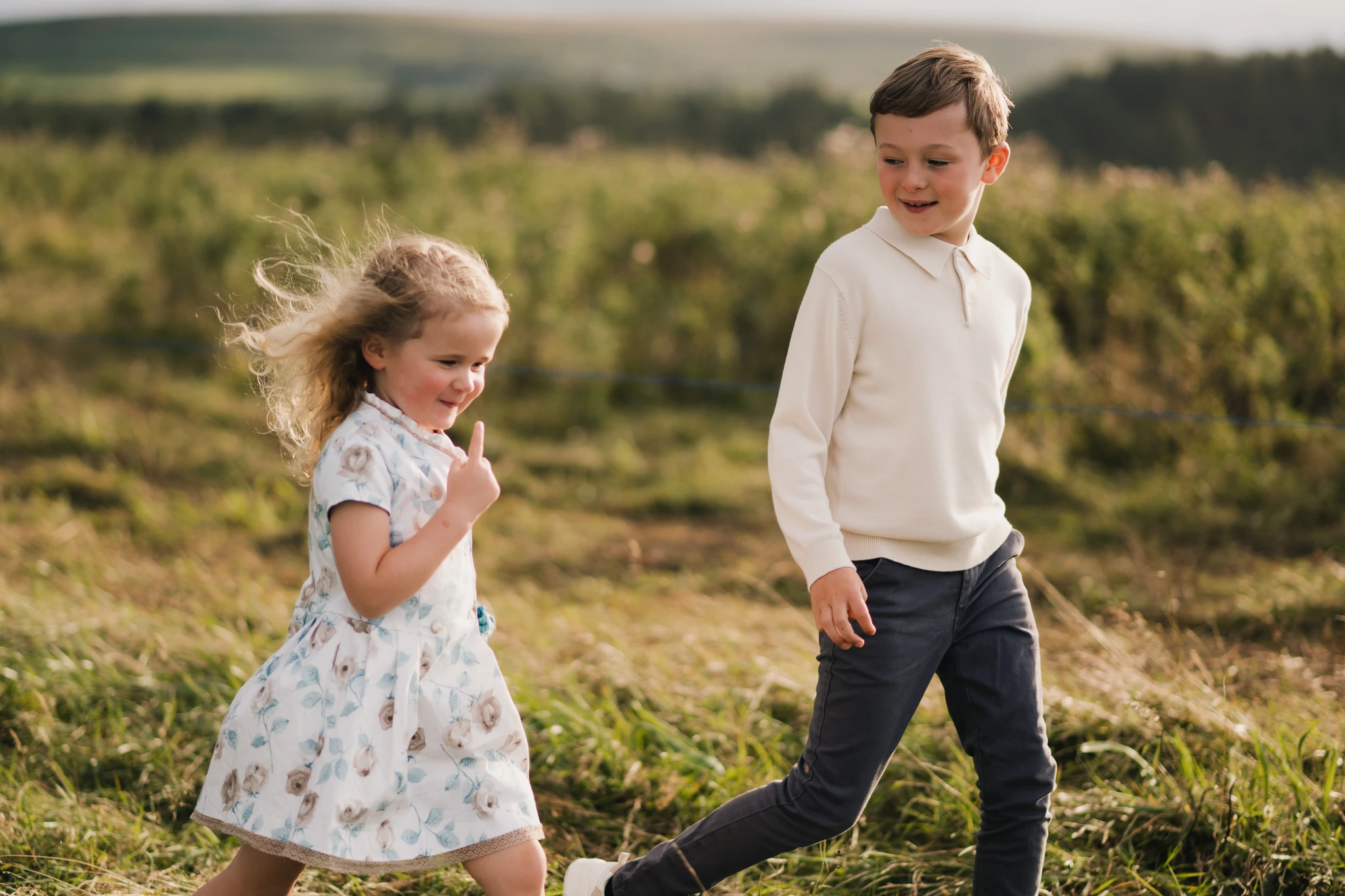 a boy and girl are running through a grassy field