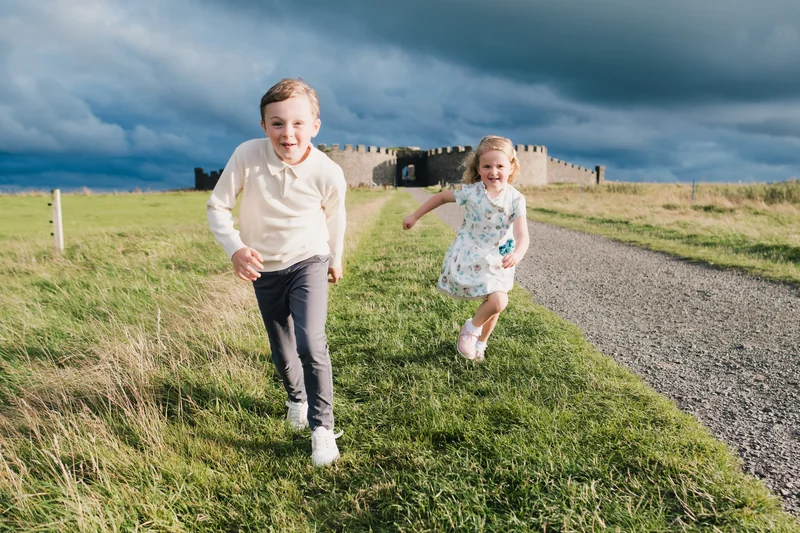 two children running down a grassy path with a castle in the background