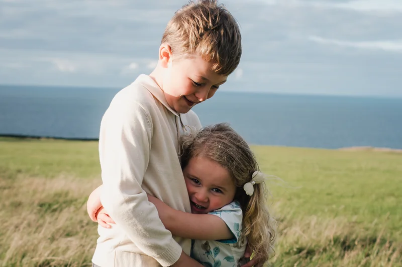 a boy and girl hugging each other in a grassy field