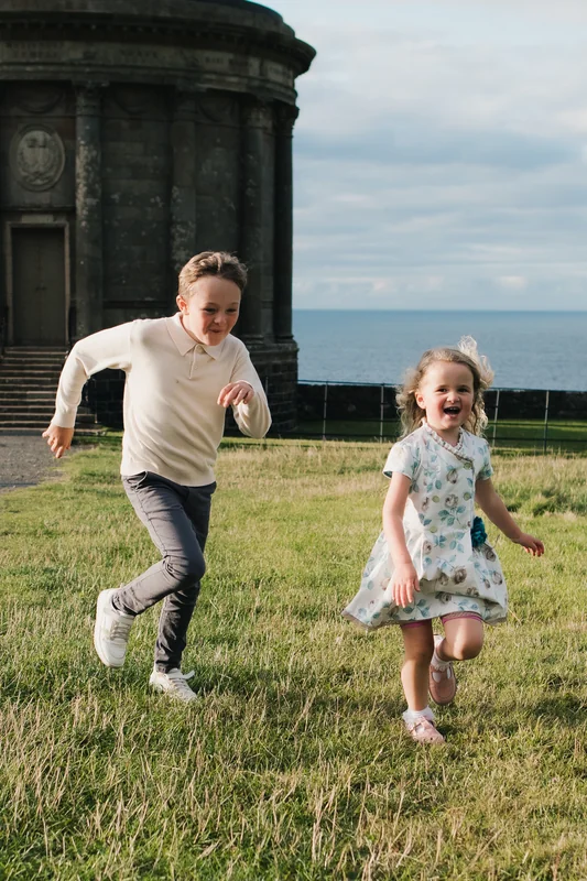 a family portrait of a girl and boy playing in a grassy field with a castle in the background