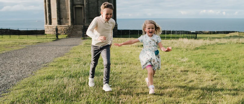 a family portrait of a mother and daughter playing in a grassy field with a castle in the background