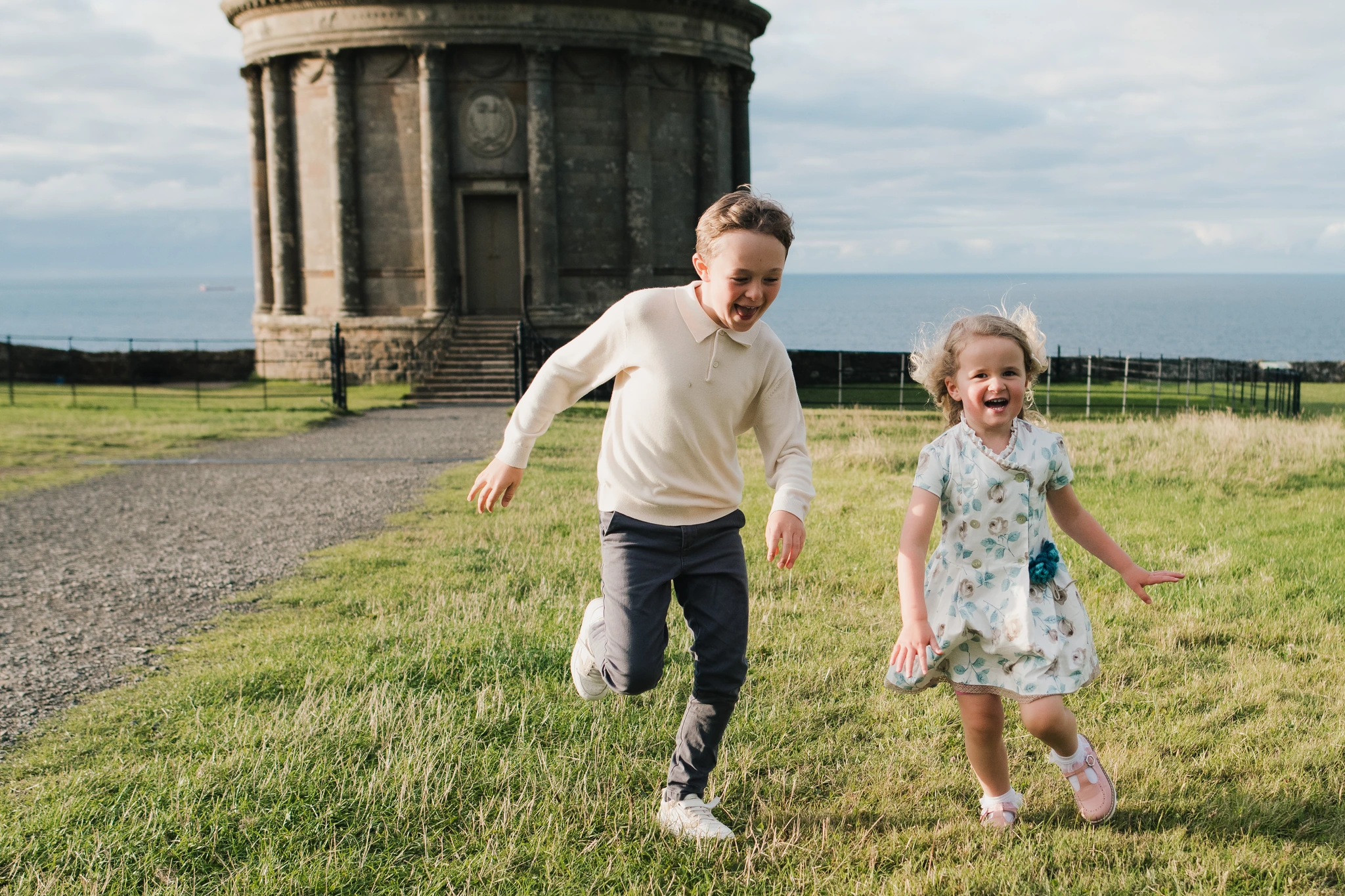 two children play in a grassy field with a large stone building in the background