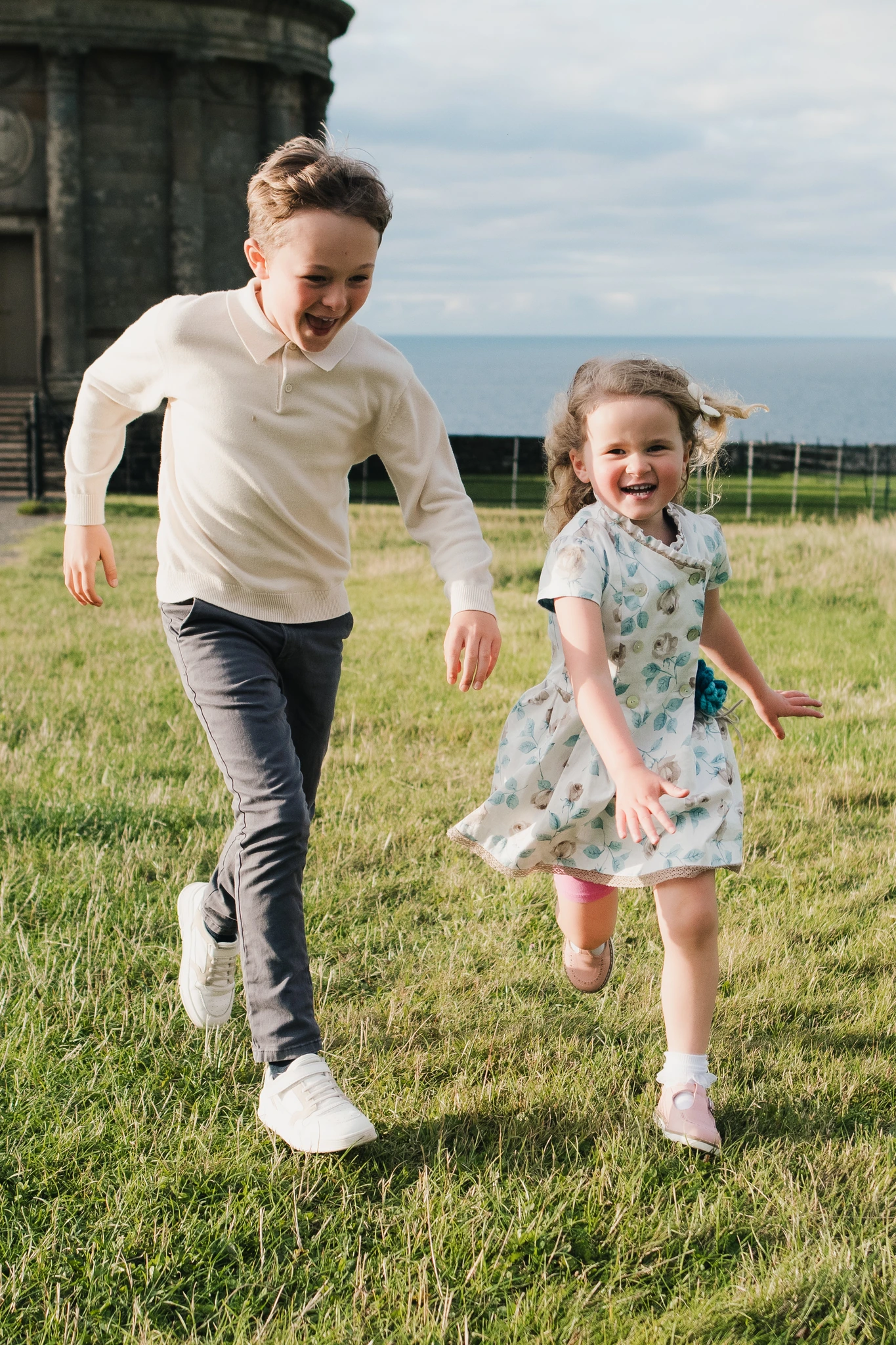 a boy and girl playing in the grass near a castle