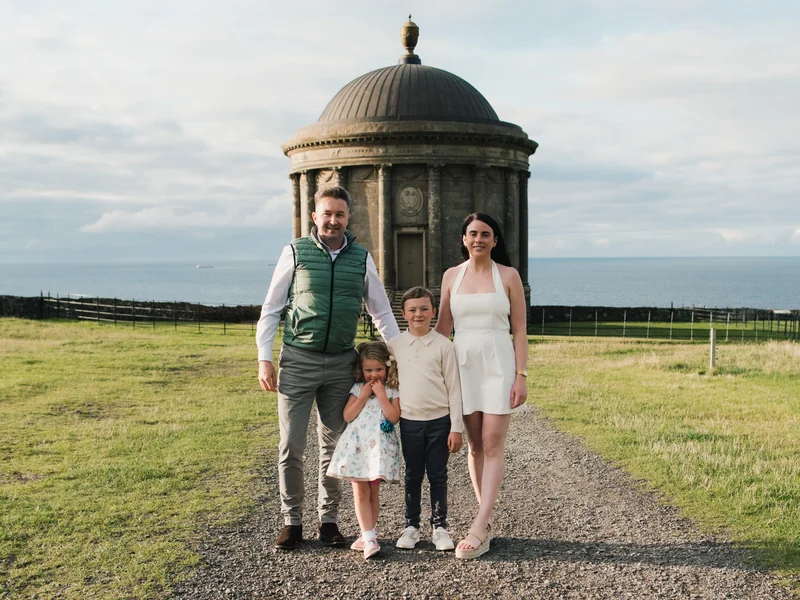 a family poses in front of a building with a tree in the background