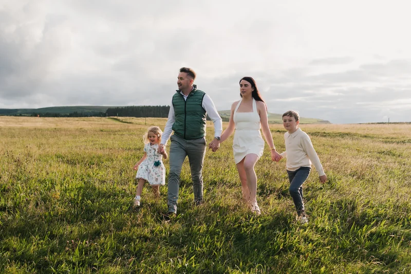 a couple and their children walk through a grassy field in front of a cloudy sky