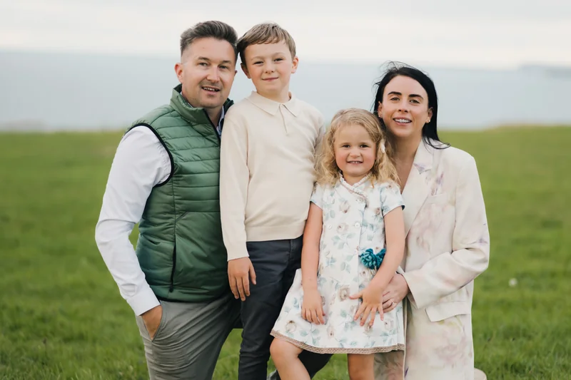 a man and woman pose for a family photo in a field with their children