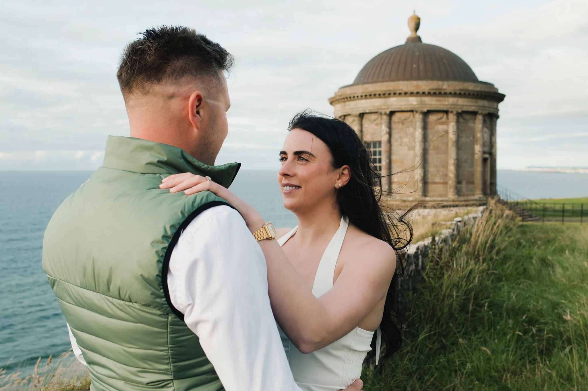 a bride and groom hugging in front of a castle overlooking the sea