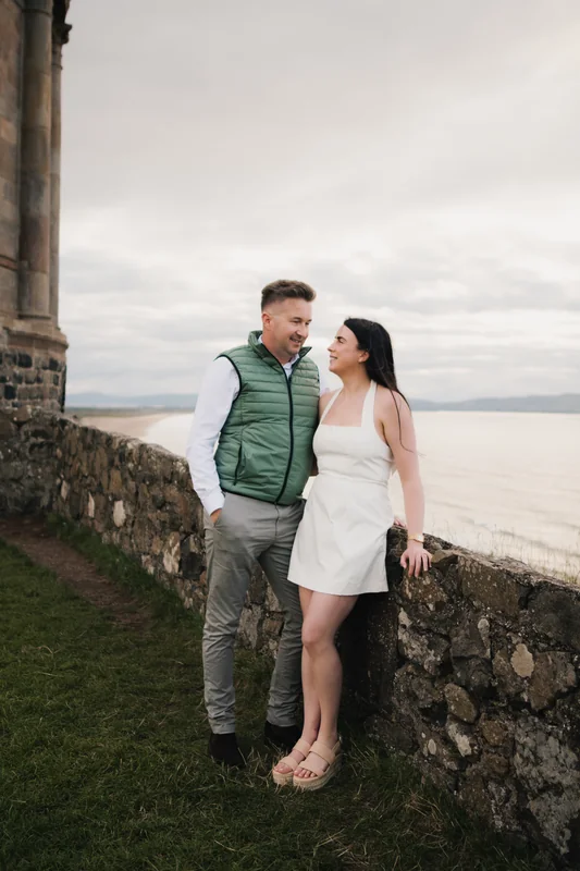 a bride and groom pose in front of a castle wall during their engagement session