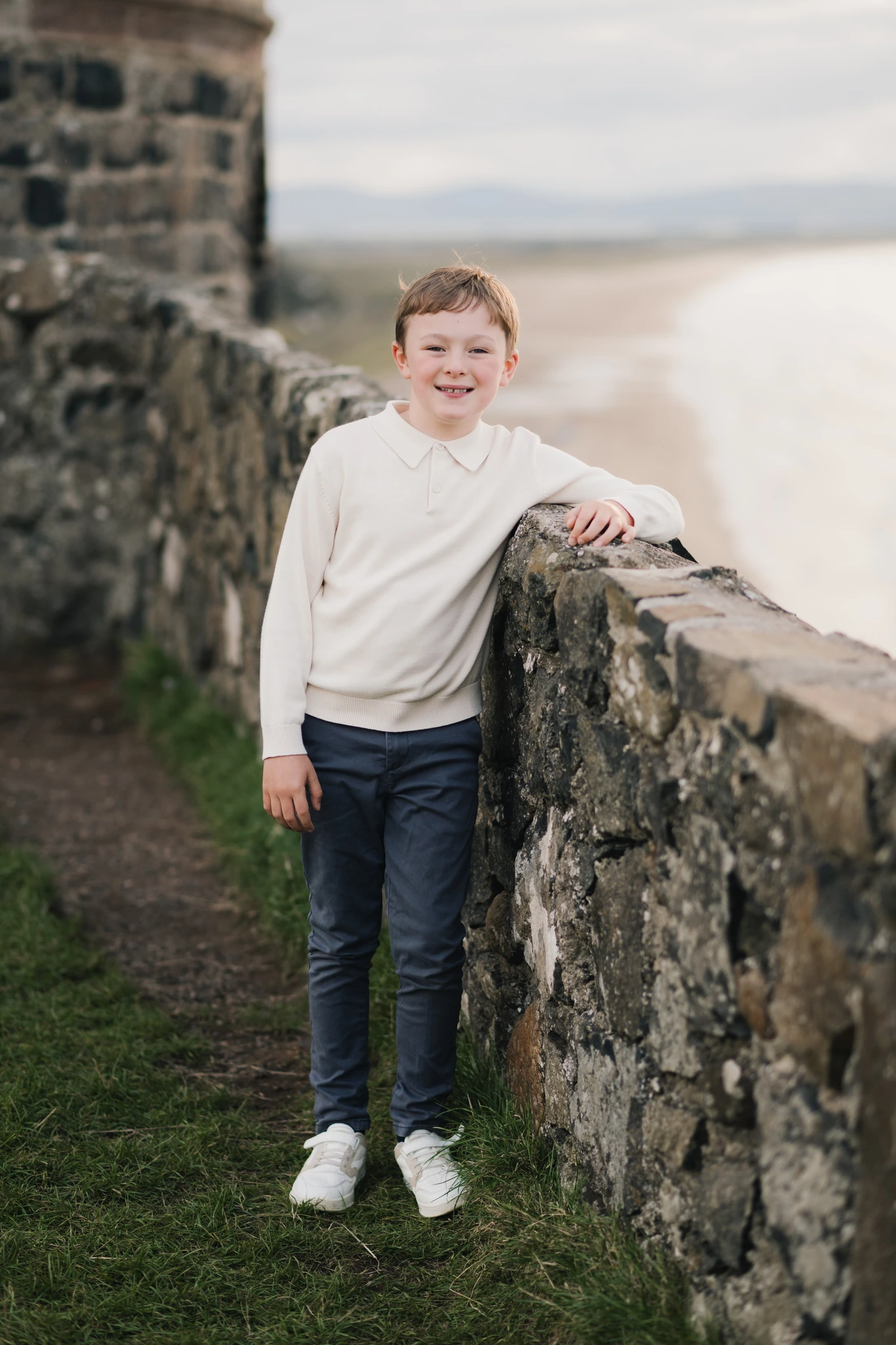a young boy leaning against a wall in front of a castle