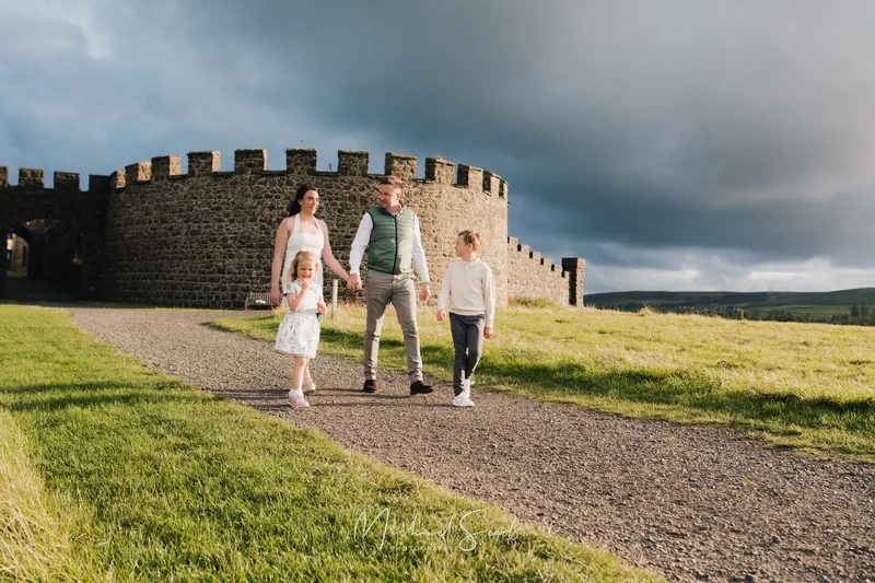 a family is walking down a path in front of a castle wall