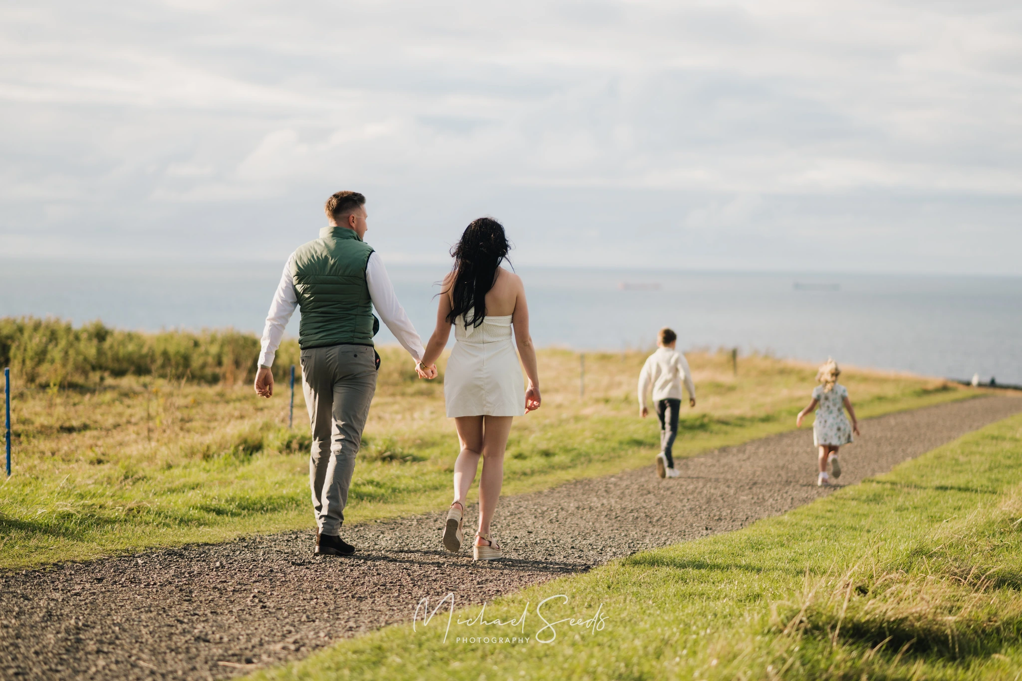 a bride and groom walk down a path towards the sea