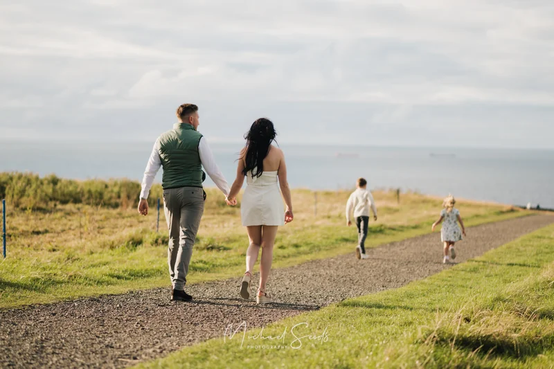 a bride and groom walk down a path towards the sea
