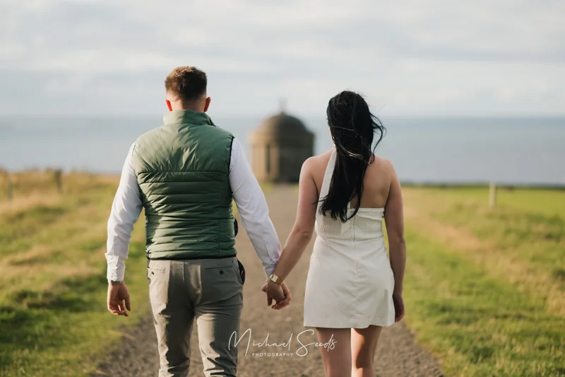 a couple holds hands as they walk down a path