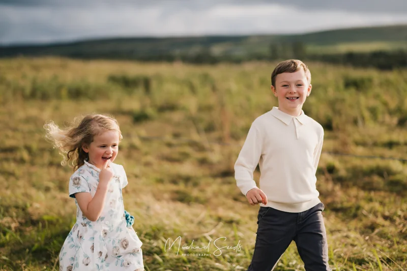 a boy and girl play in a grassy field with a cloudy sky