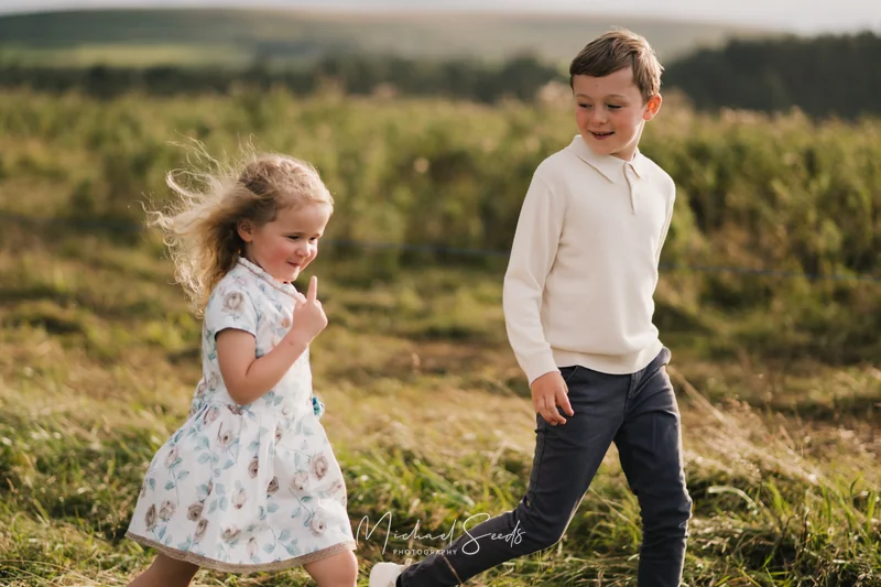 a boy and girl are running through a field of grass