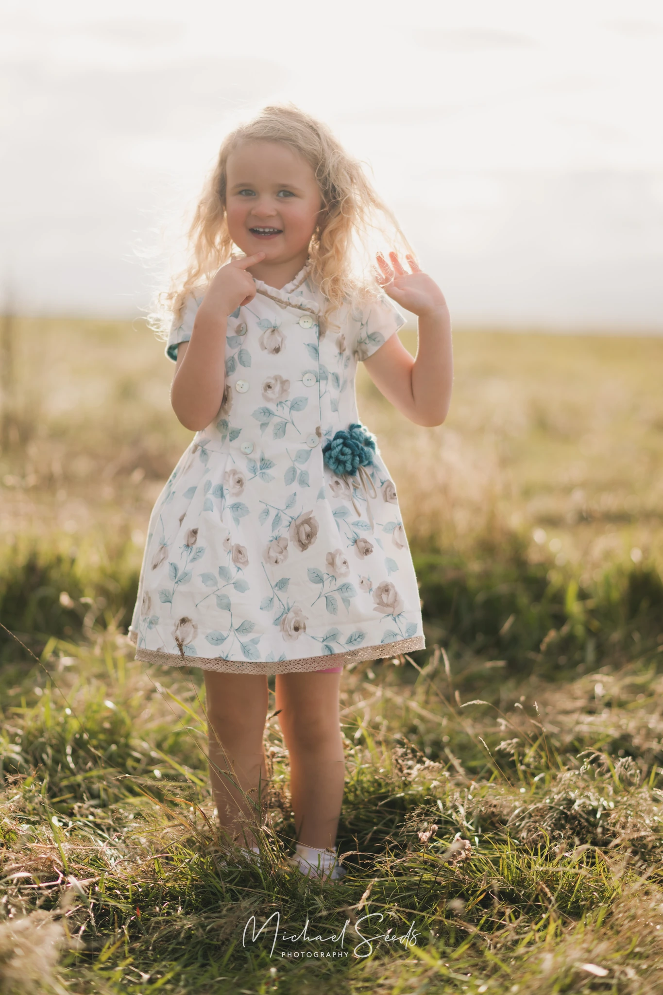 a little girl in a blue dress standing in grass with a smile on her face