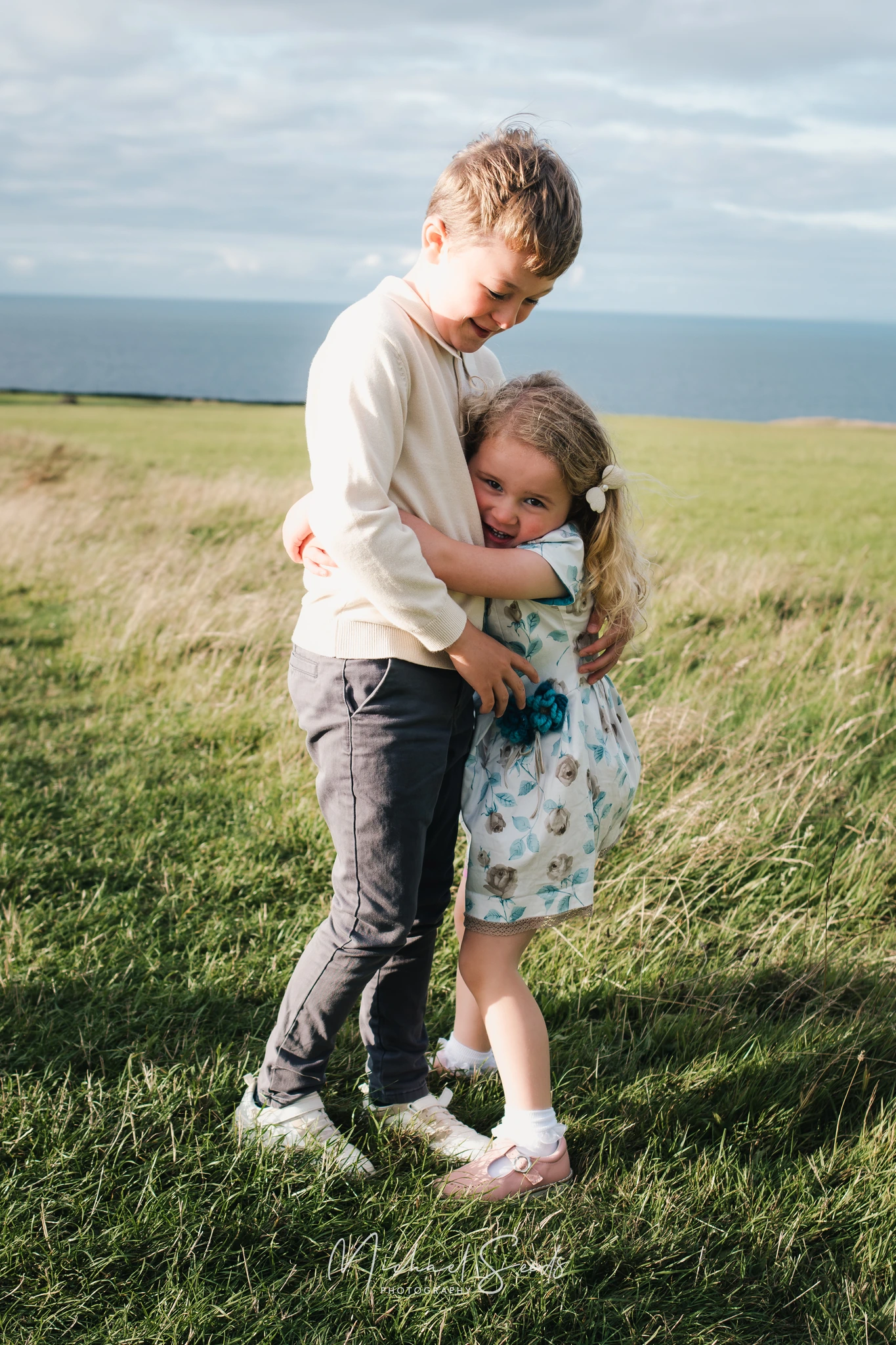two children hugging on a grassy hillside