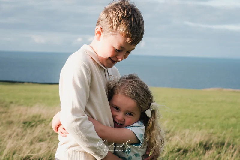 a boy and girl hugging each other in a grassy field