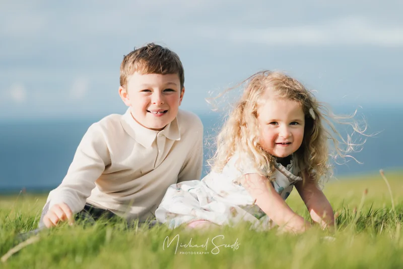 two children play on the grass in front of a blue sky