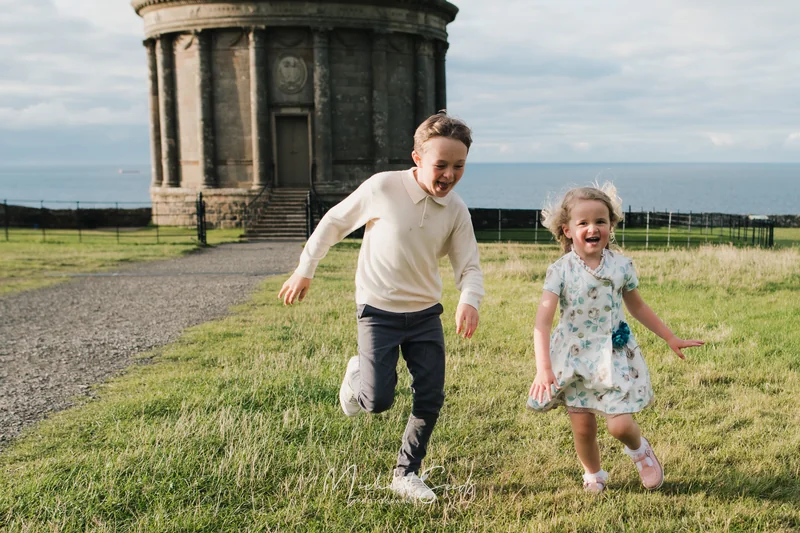 two children play in a grassy field with a large stone building in the background