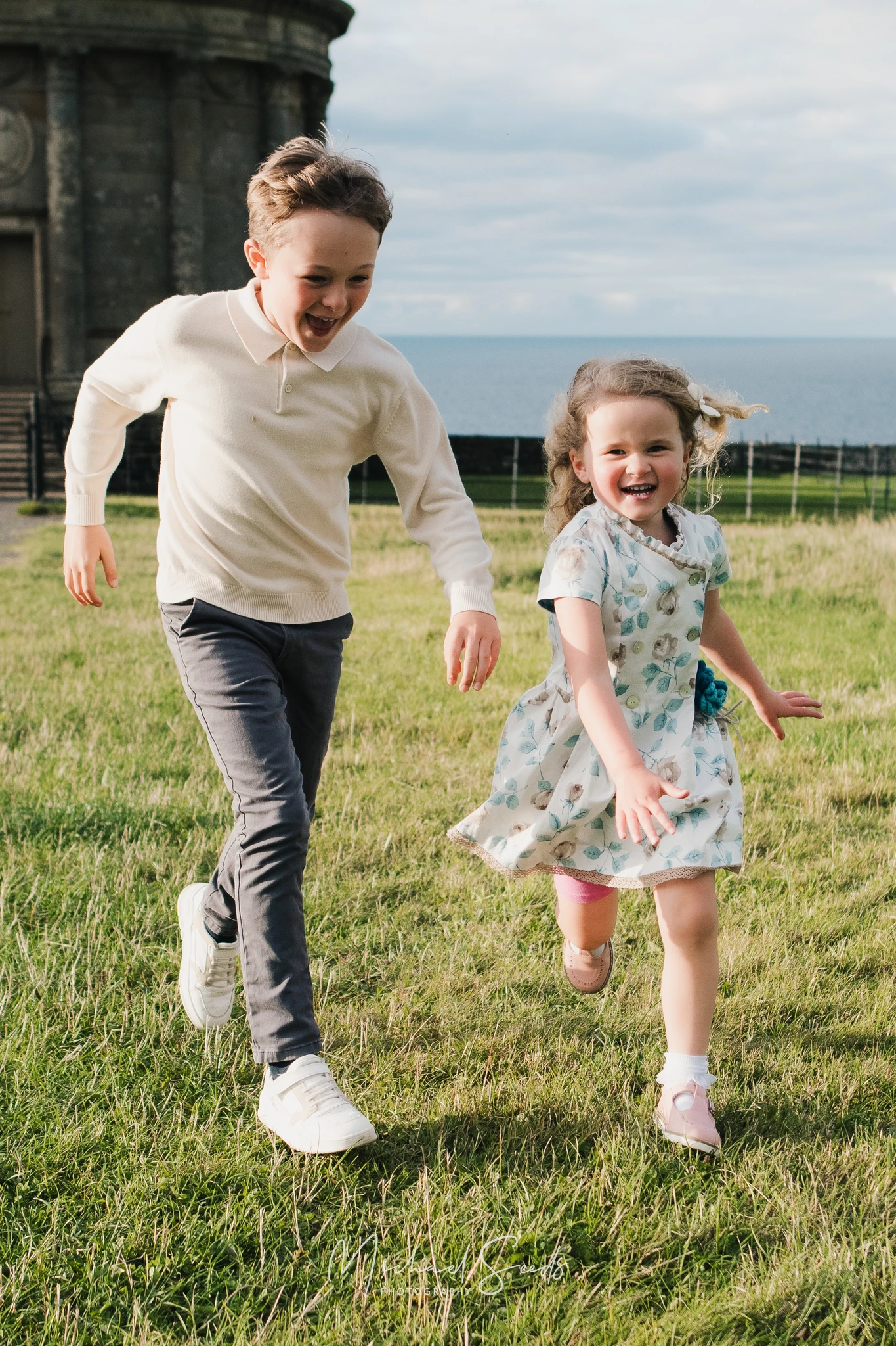 a boy and girl playing in the grass near a castle