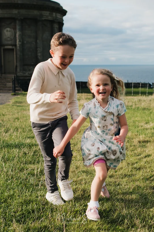 a family portrait of a boy and a girl in a grassy field with a castle in the background