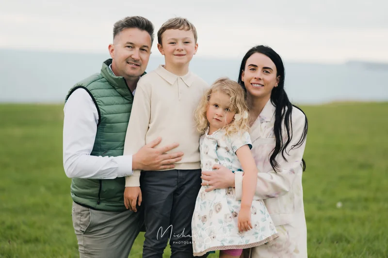 a man and a woman pose with their children in a grassy field