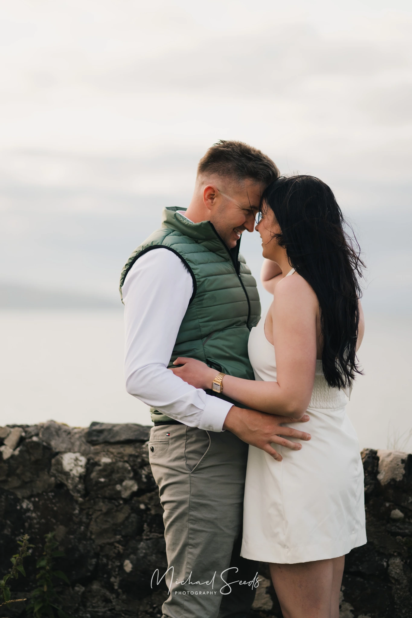 a bride and groom hugging on a stone wall in ireland