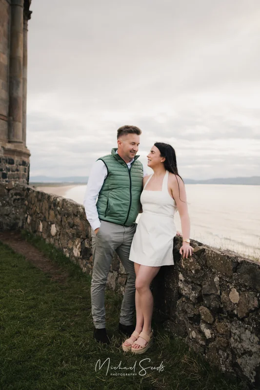 a bride and groom pose in front of a castle wall during their engagement session