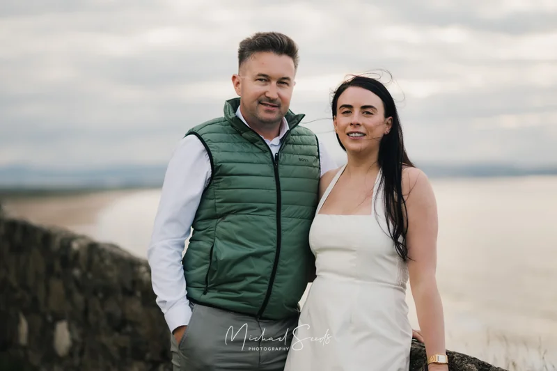 a man and woman standing next to a wall with a view of the sea