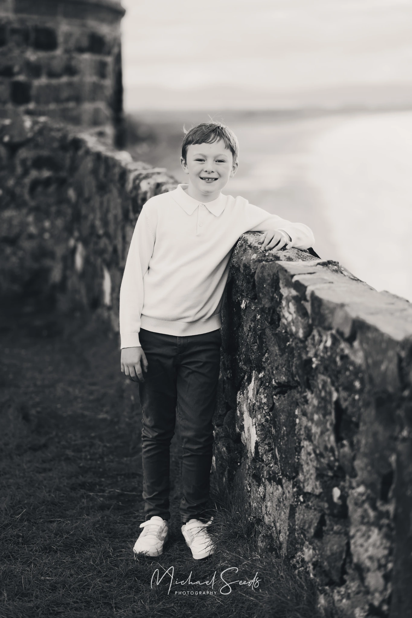 black and white portrait of a young boy leaning against a wall