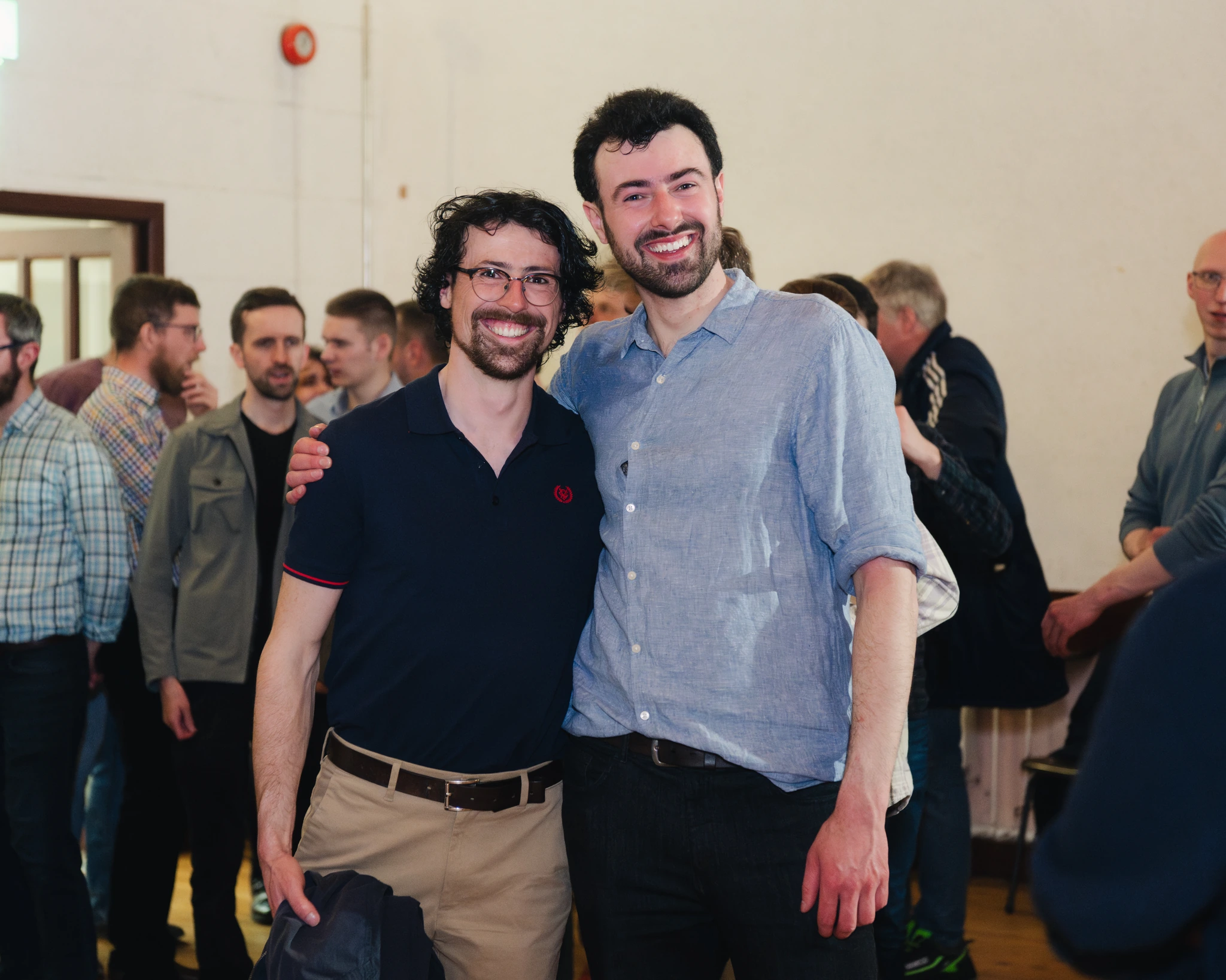 two men standing next to each other in a room full of people