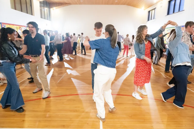 a group of people dancing on a wooden floor in a gymnasium