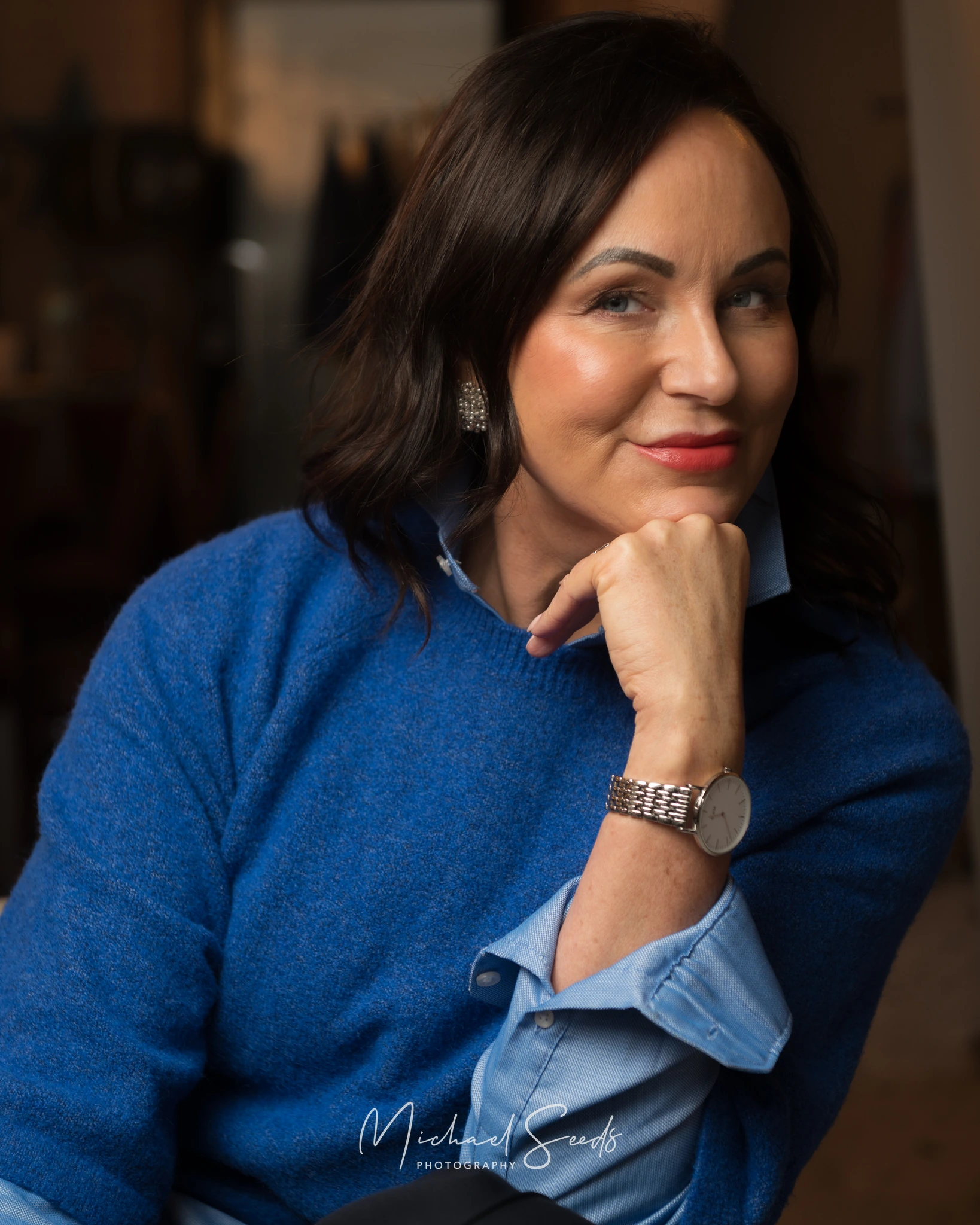 a woman in a blue sweater sitting on a chair with her hands on her lap