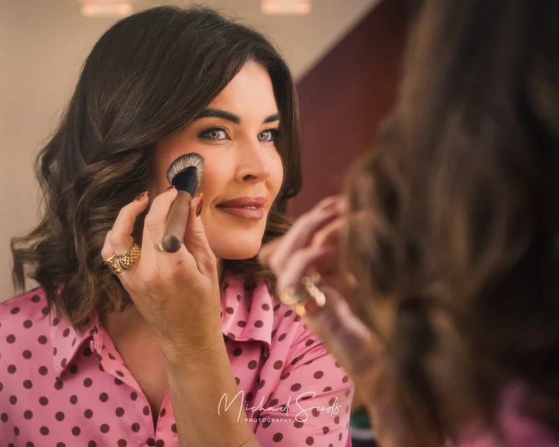 a woman wearing a pink shirt is applying makeup in front of a mirror