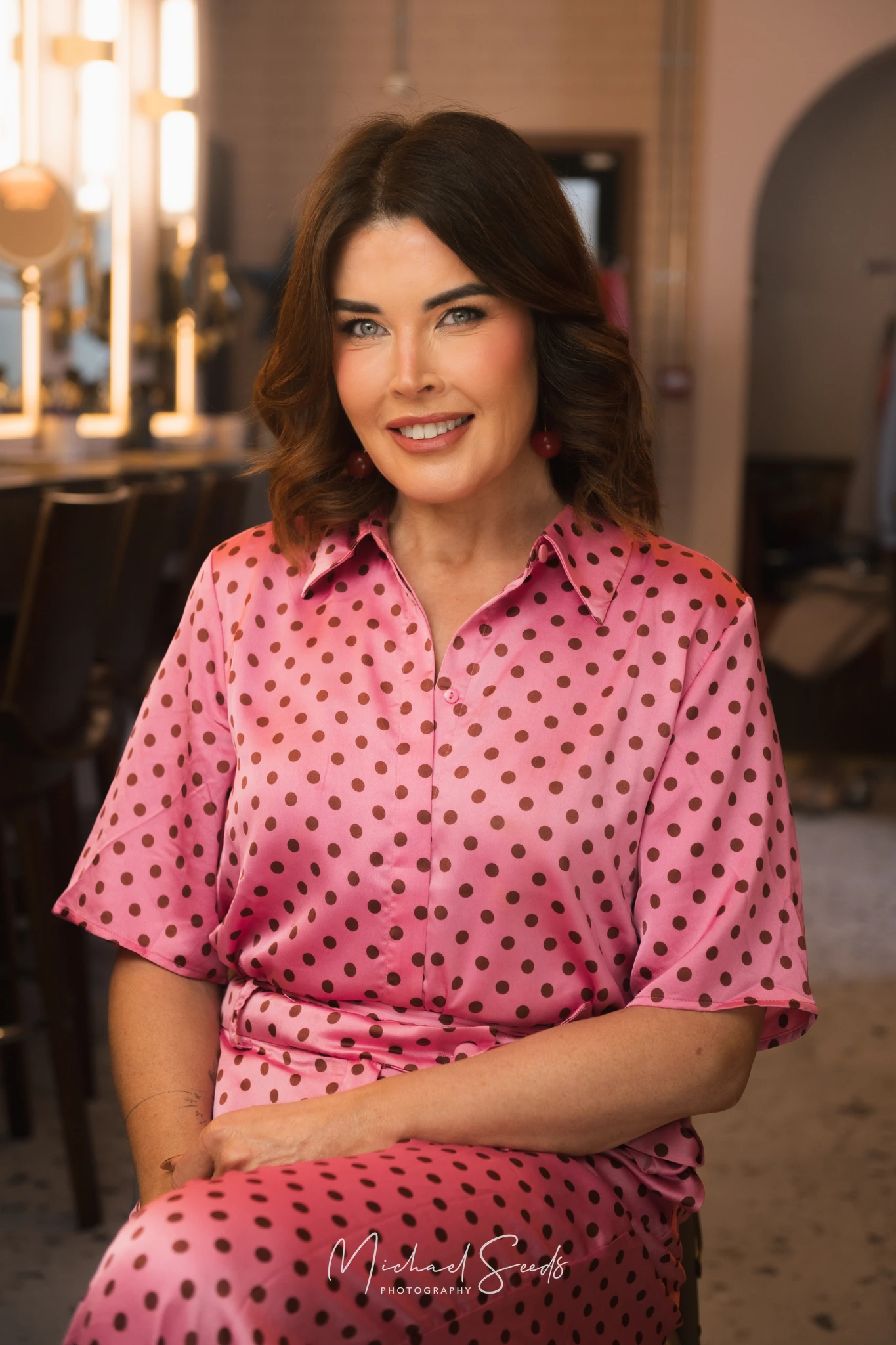 a woman in a pink polka dot dress sitting on a stool