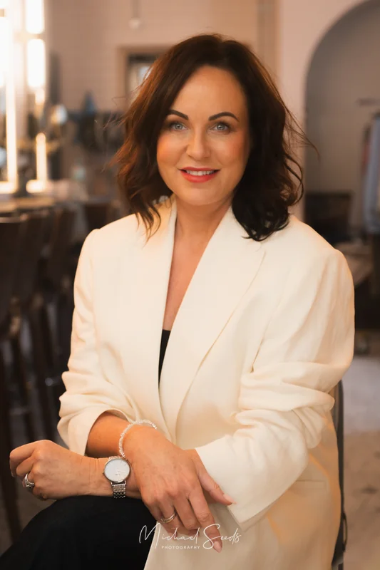 a woman in a white blazer and white blouse sitting on a chair