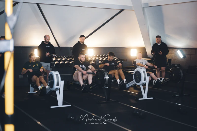 a group of people sitting on a rowing machine in a gym