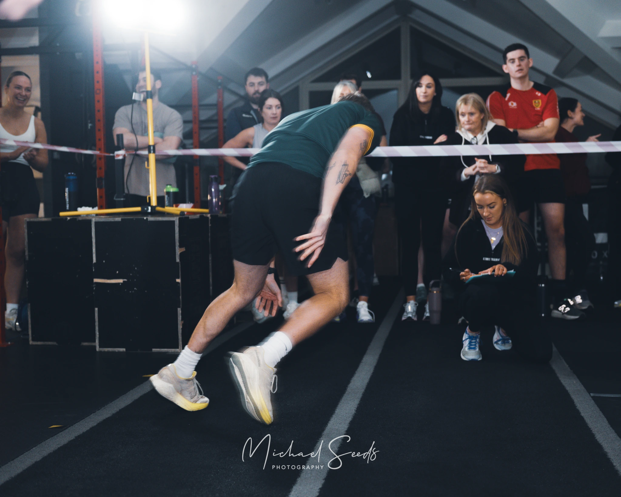 a man kicking a tennis ball in front of a group of people in a gym