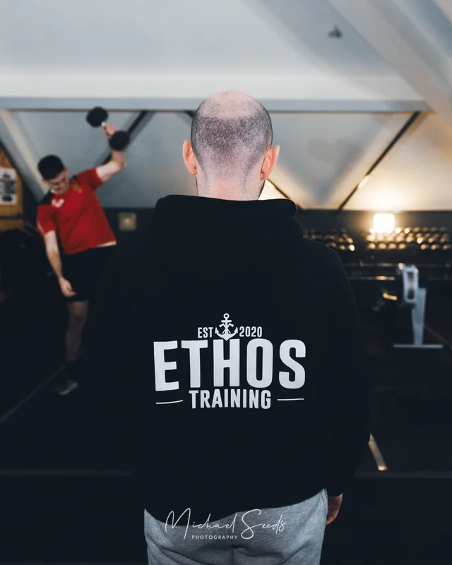 a man in a gym wearing a black hoodie with the words ethos training