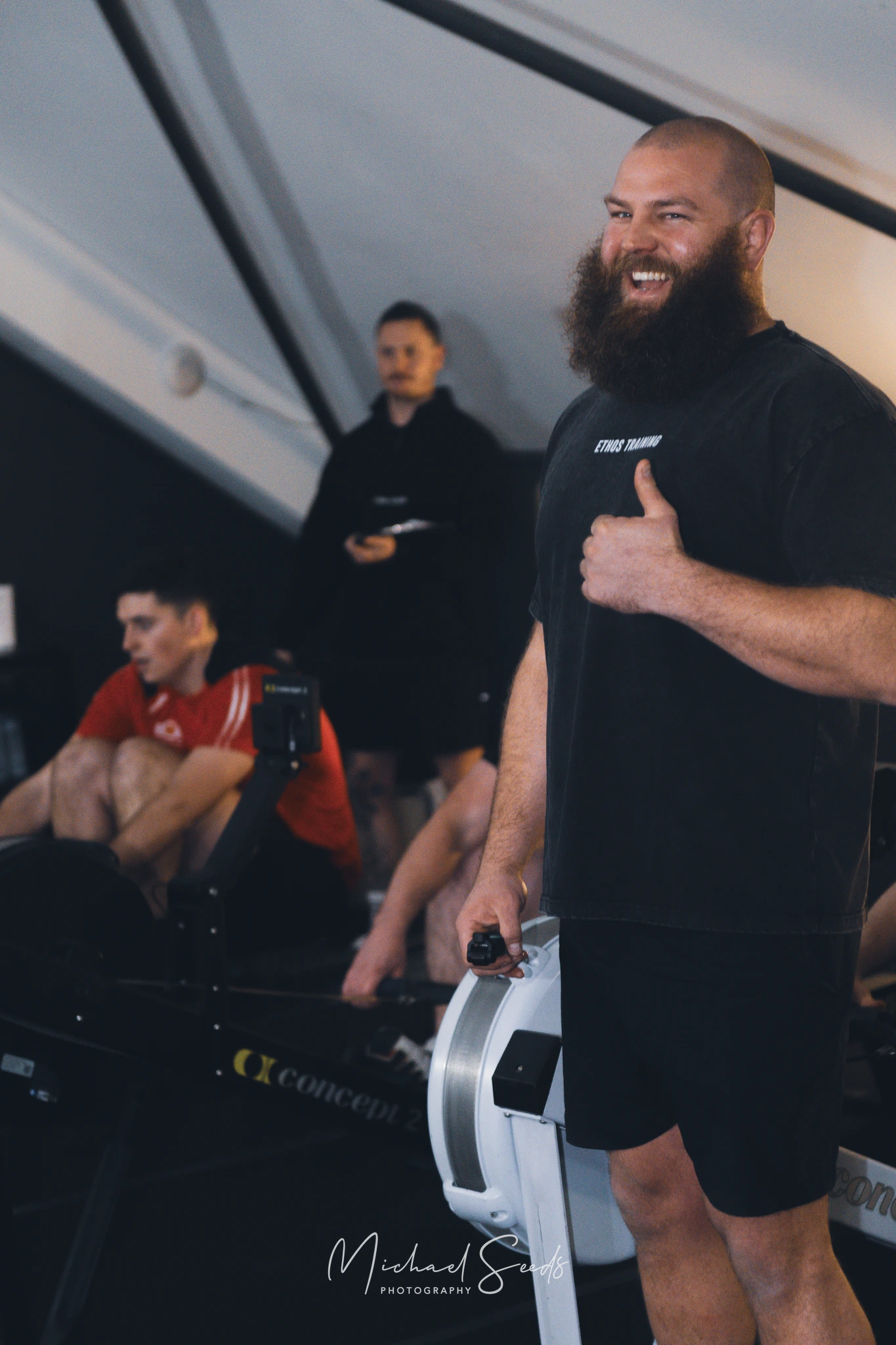 a man with a beard and moustache standing in front of a rowing machine