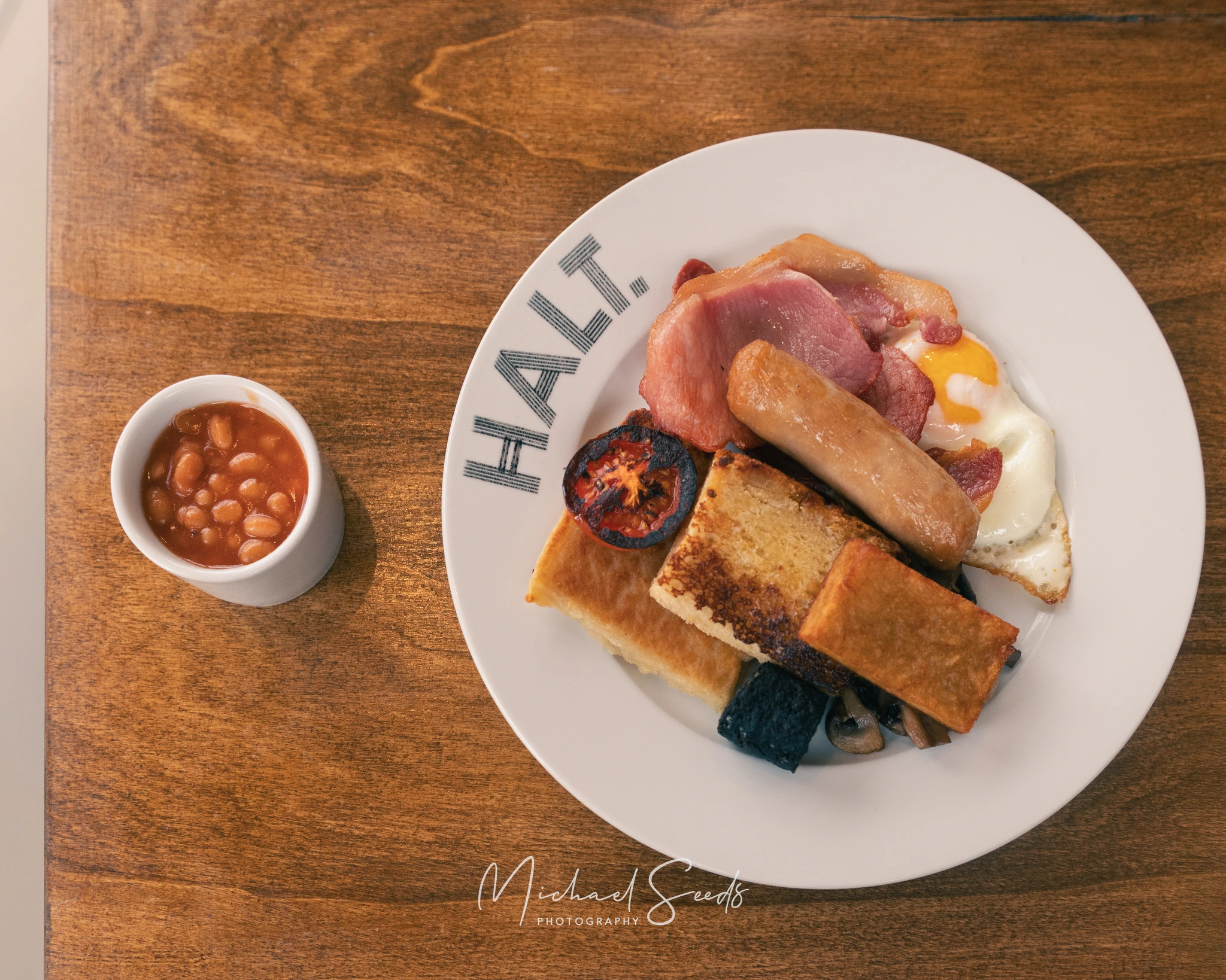 a plate with eggs, bacon, sausages and toast on a wooden table