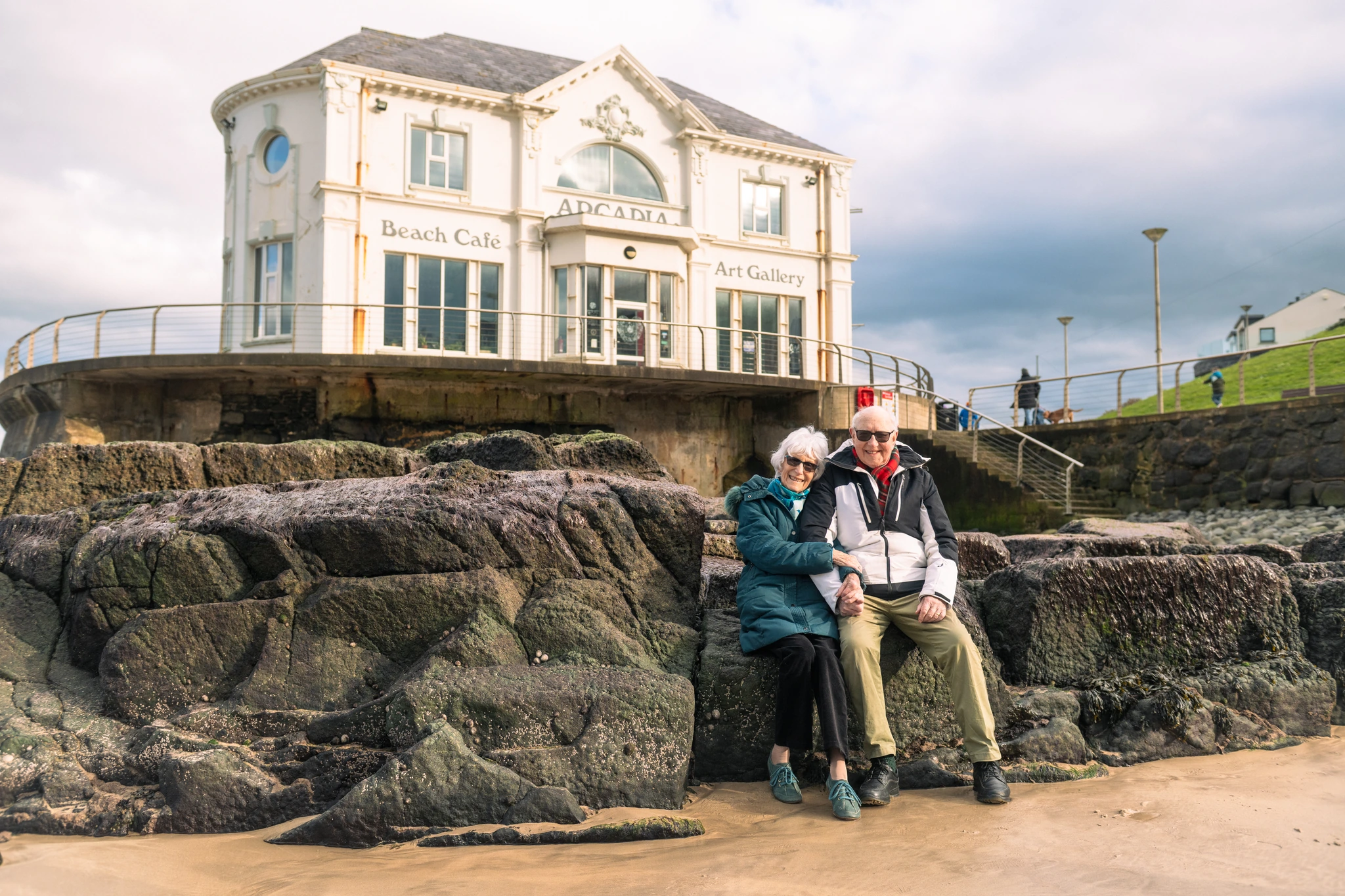 a couple sits on rocks in front of a lighthouse