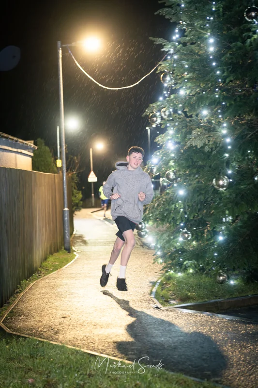 a man running down a street at night with a christmas tree in the background