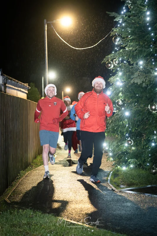 a group of people dressed in santa hats running around a christmas tree at night