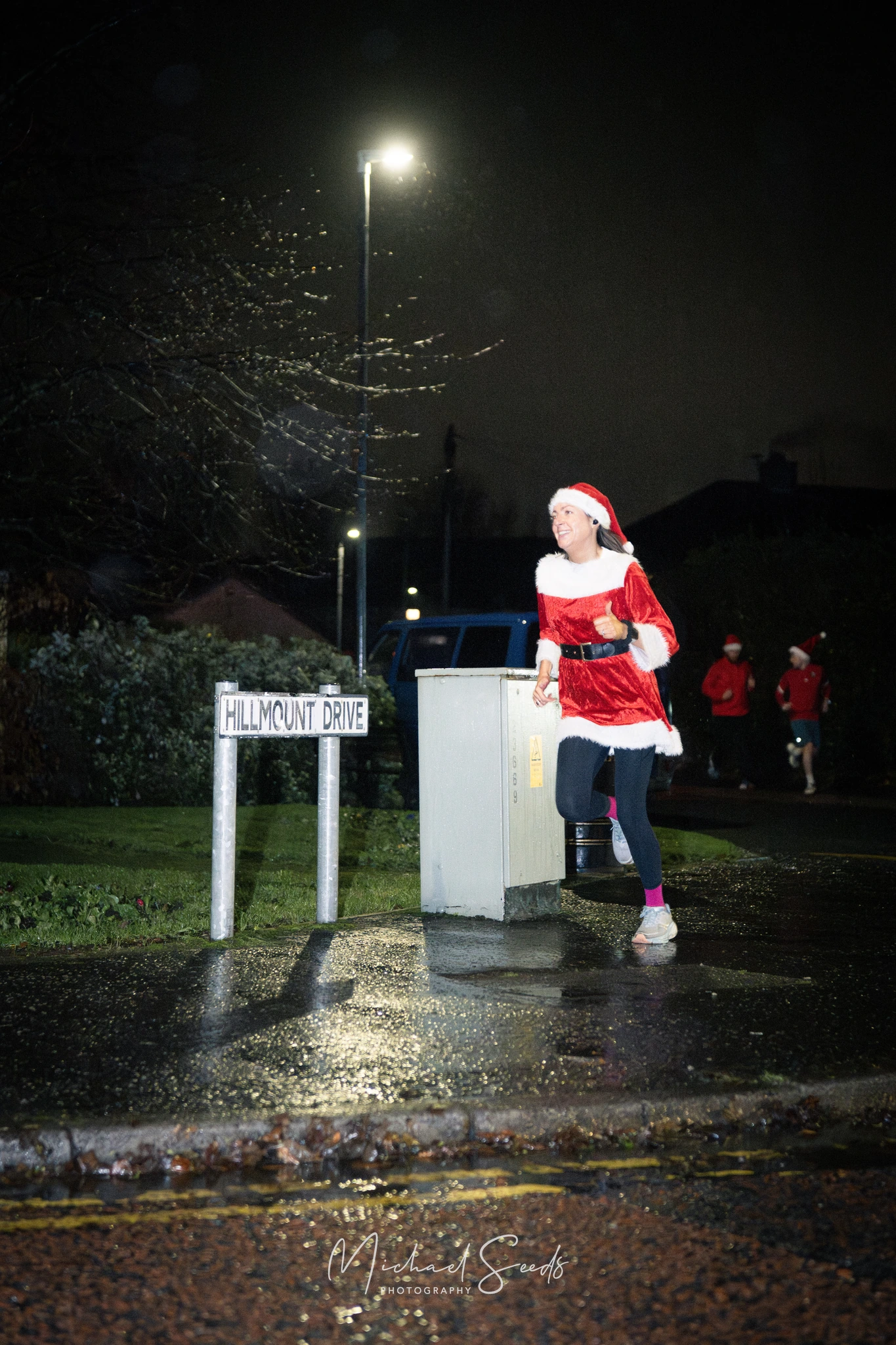 a woman dressed as santa runs down a street at night