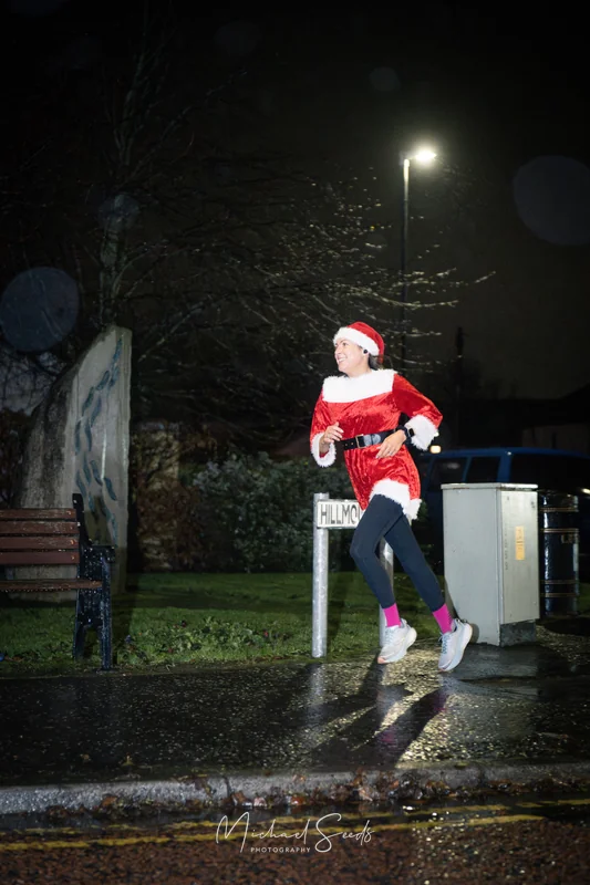 a woman dressed as santa running down a street at night