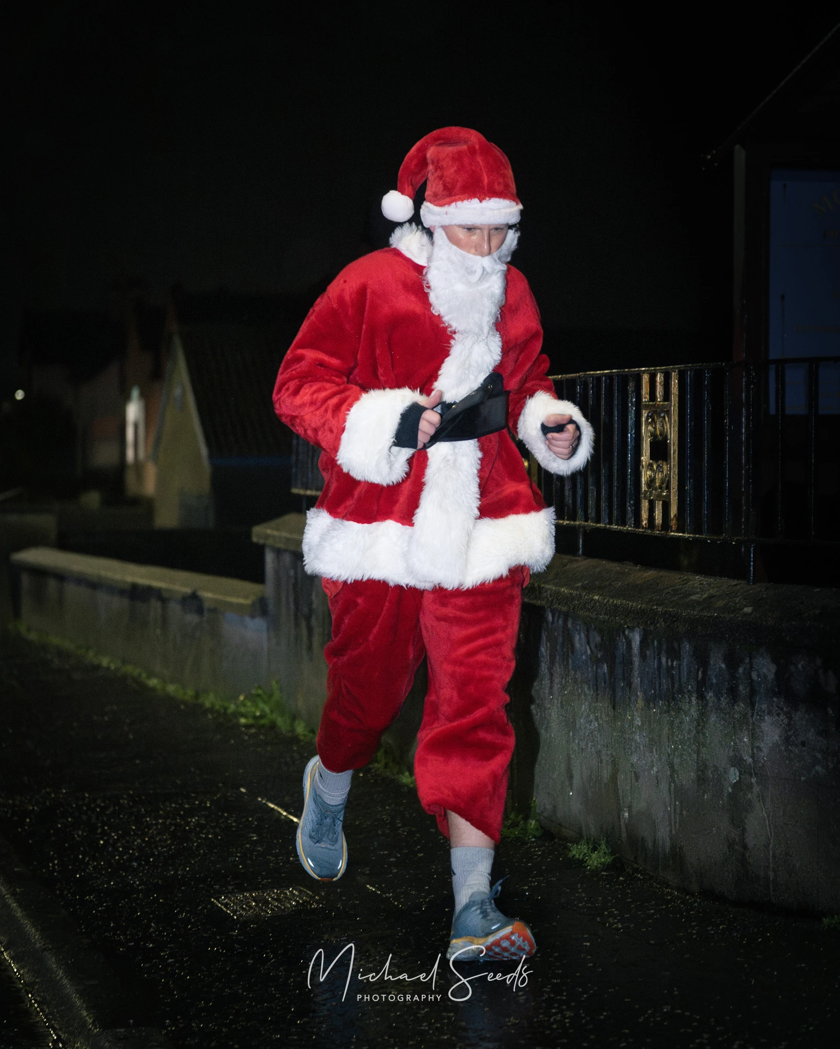 a man dressed as santa runs down a street at night