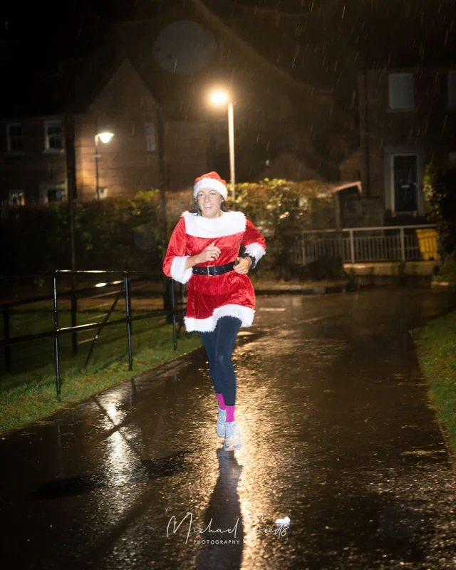 a woman dressed as santa running in the rain