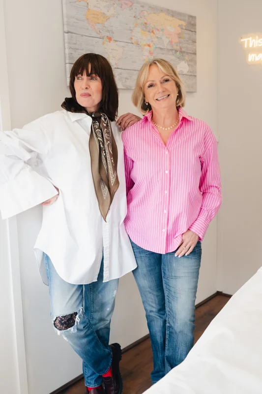 two women standing next to each other in front of a bed in a hotel room